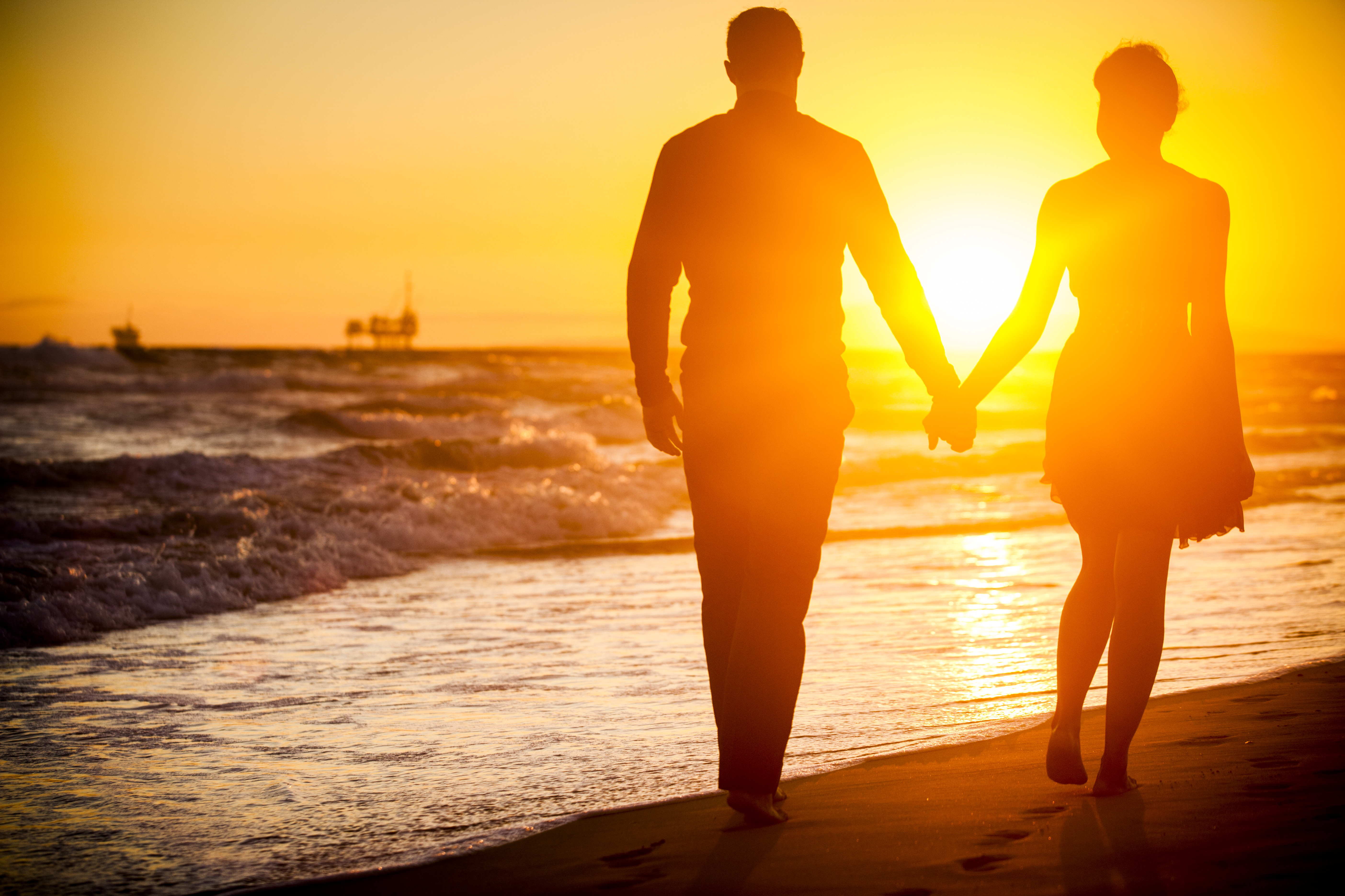 Diverse couple walking on beach at sunset