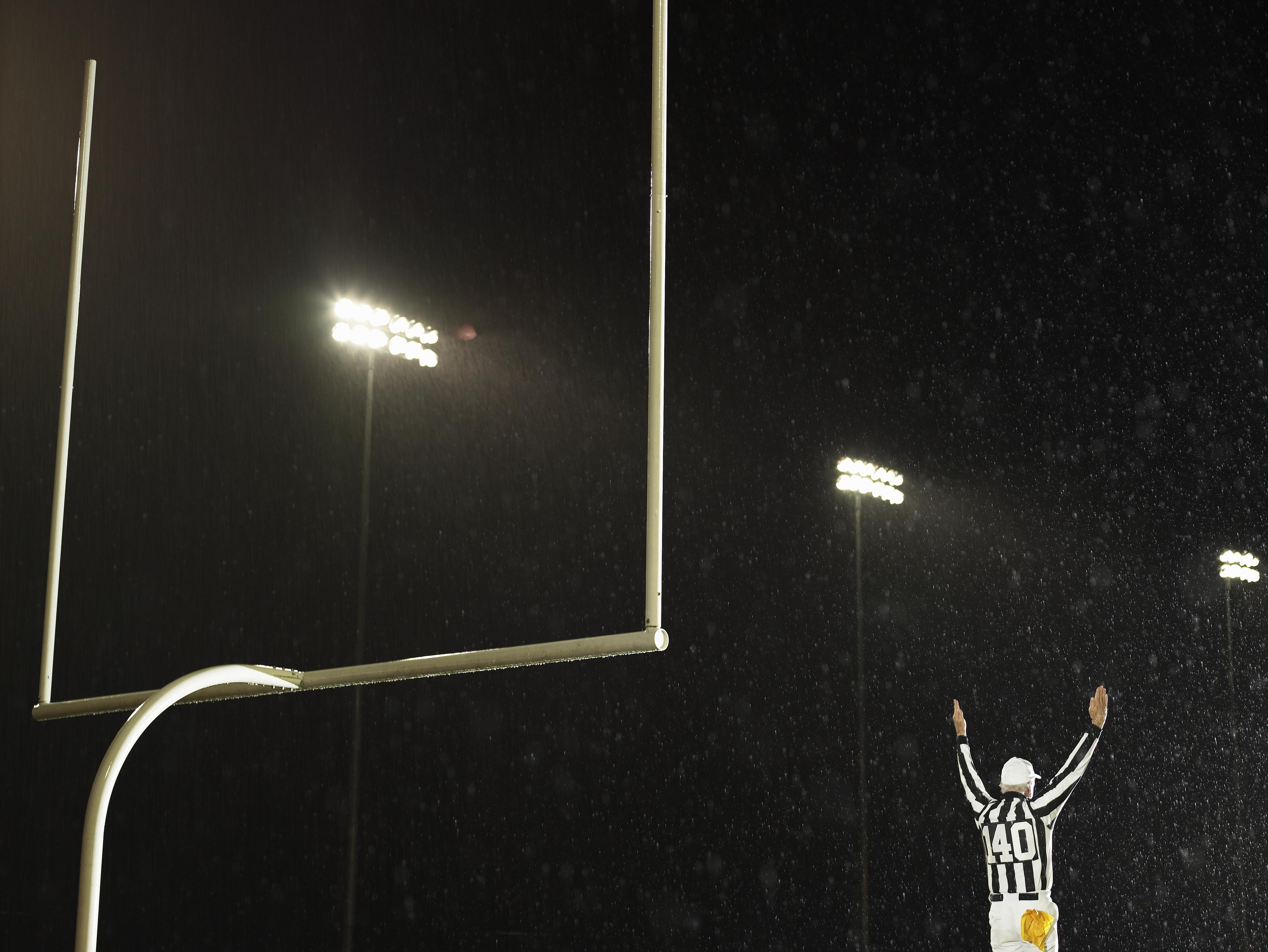 American football referee giving touchdown signal, rear view